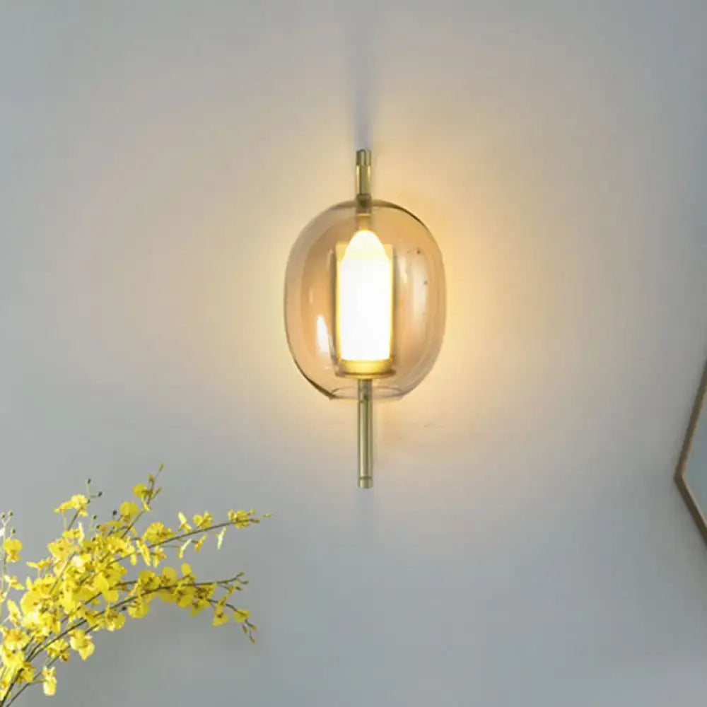 Modern brass wall sconce featuring a warm-toned amber oval clear glass globe with a sleek minimalist brass finish