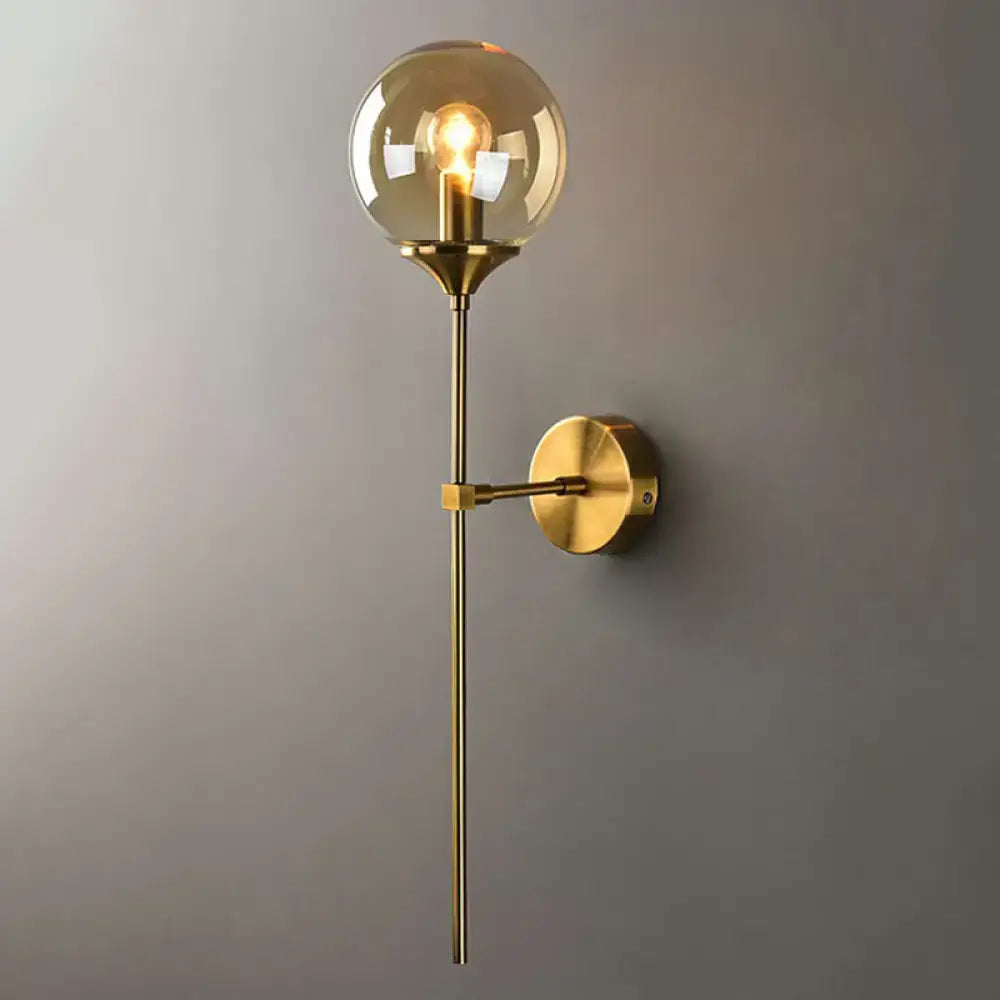 Modern brass pencil arm wall light featuring a gold-toned metal arm and spherical amber glass globe sconce