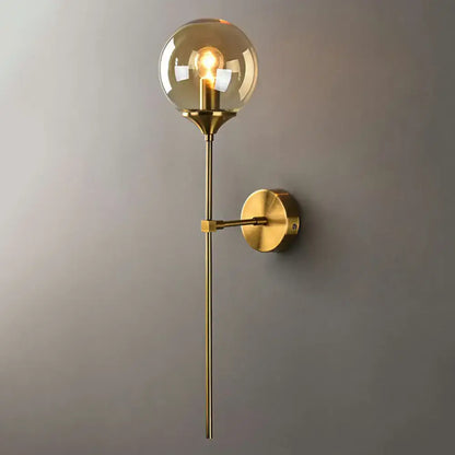 Modern brass pencil arm wall light featuring a gold-toned metal arm and spherical amber glass globe sconce