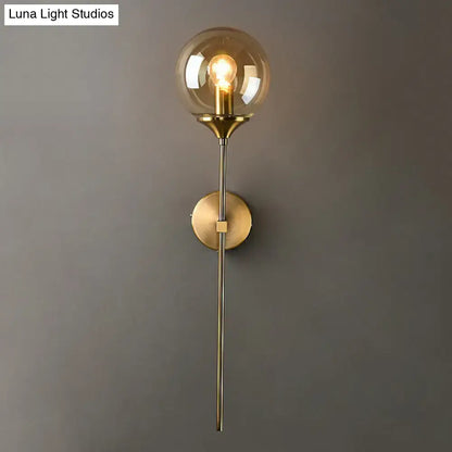 Modern brass pencil arm wall light with gold-toned metal stem and smoke gray spherical glass globe for bedroom use