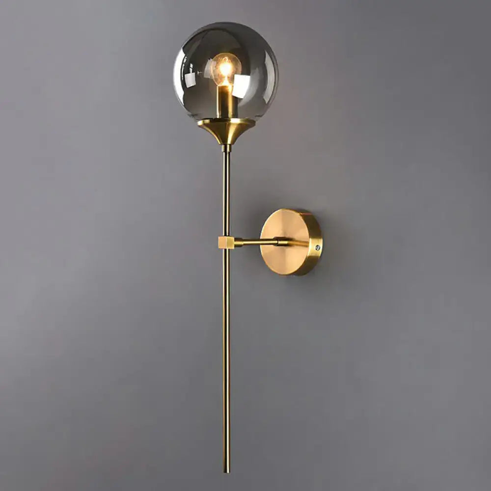 Modern brass pencil arm wall light with gold-toned metal stem and smoke gray glass globe for bedroom use