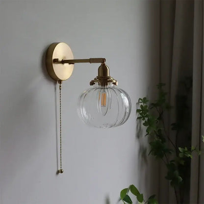 Modern brass wall sconce with decorbites glass ball, ribbed globe, edison bulb, and pull-chain switch for bedroom light