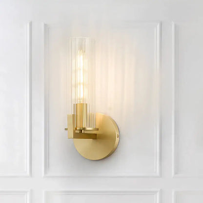 Modern brass wall sconce with a gold-toned finish and clear ribbed glass shade featuring an exposed filament bulb