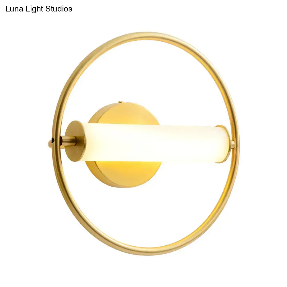 Modern brass ring wall sconce with gold-toned finish and illuminated opal glass shade for bedroom lighting