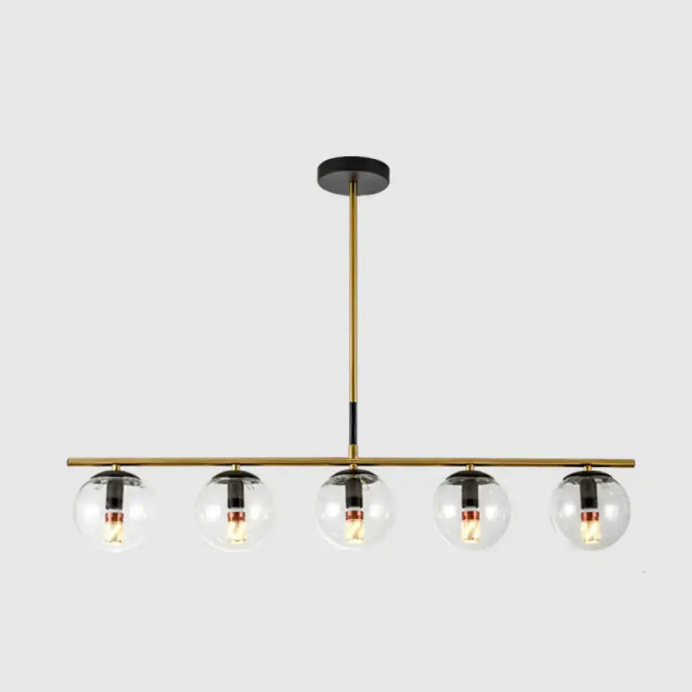 Modern brass and smoke grey globe chandelier with five clear glass globes and black accents for kitchen island lighting