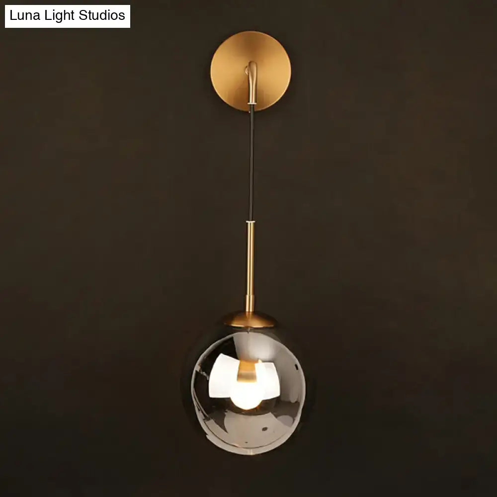 A sleek modern brass glass ball wall hanging lamp with a smoked glass globe for bedroom lighting