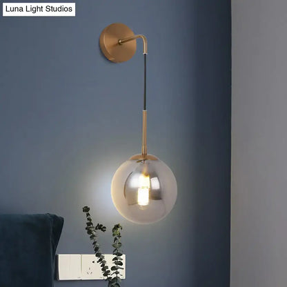 Modern brass wall hanging lamp with a gold-toned stem and spherical smoked glass ball wall shade for bedroom lighting
