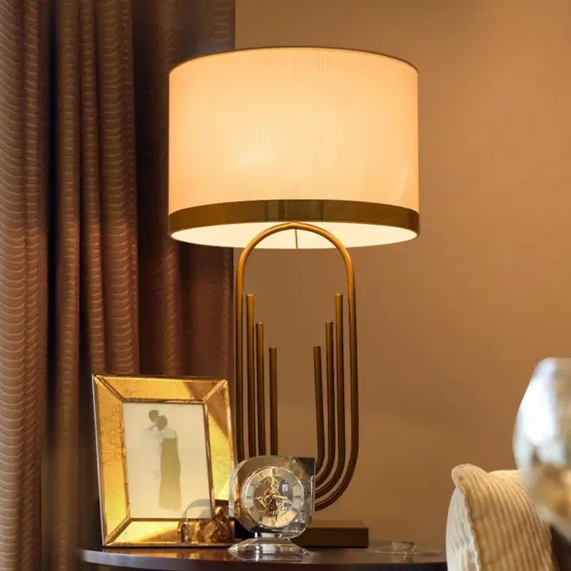 Modern brass table lamp with gold paperclip design and off-white fabric shade by decorbites brass for bedroom decor