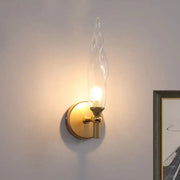 Modern brass torch sconce featuring a gold-toned frame and clear glass twisted shade for bedroom wall lighting