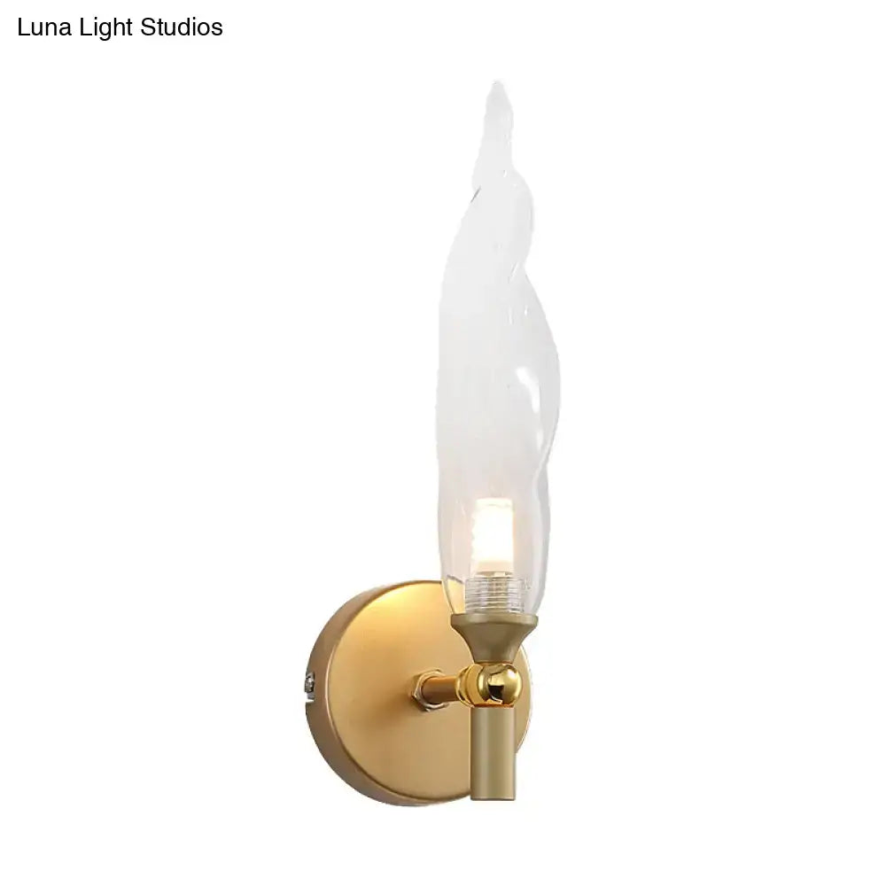 Modern brass torch sconce with gold-toned finish and clear glass flame-shaped shade for bedroom wall lighting