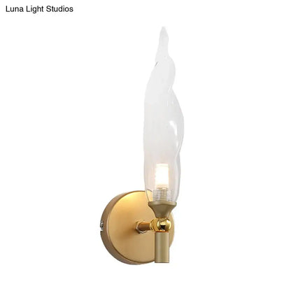 Modern brass torch sconce with gold-toned finish and clear glass flame-shaped shade for bedroom wall lighting