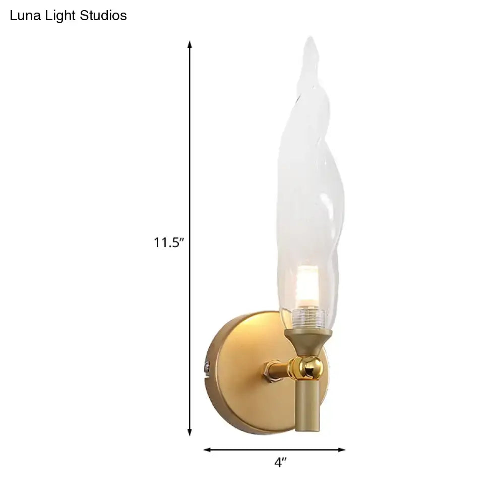 Modern brass torch sconce with clear glass flame shade and brushed gold base designed for bedroom wall lighting