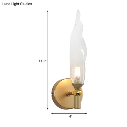 Modern brass torch sconce with clear glass flame shade and brushed gold base designed for bedroom wall lighting
