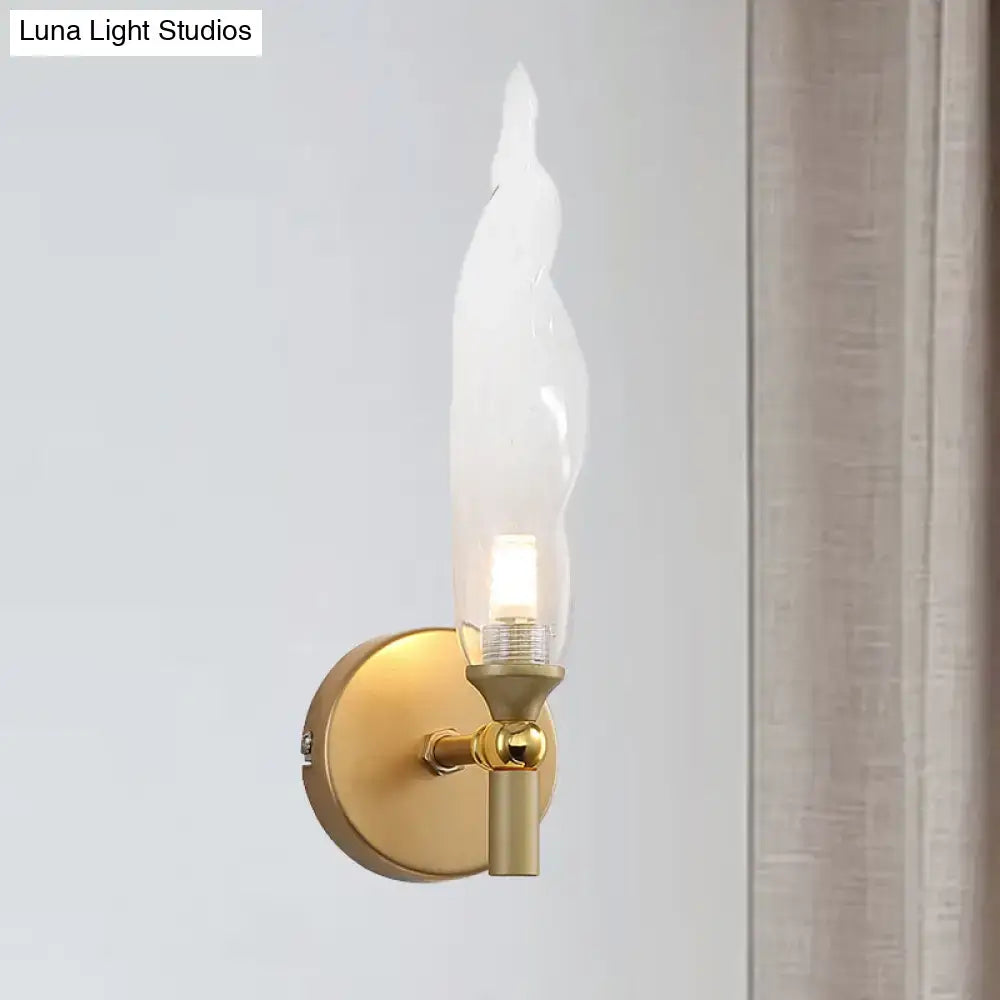 Modern brass torch sconce with a sleek gold-toned finish and clear glass flame-shaped shade for bedroom walls