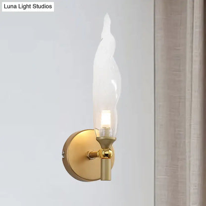 Modern brass torch sconce with a sleek gold-toned finish and clear glass flame-shaped shade for bedroom walls