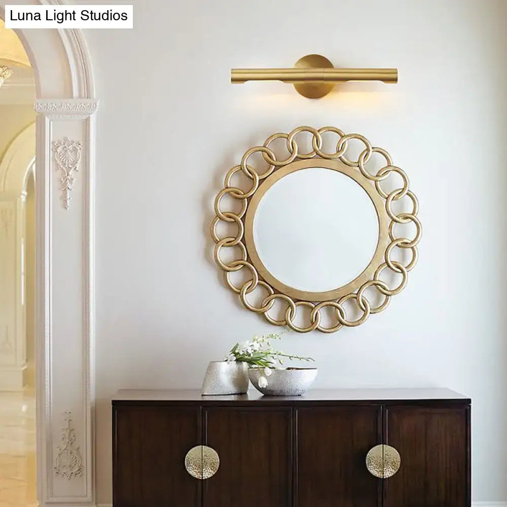 Modern brass tube vanity light featuring a gold-toned circular mirror with a decorative chain-link frame for bathroom use