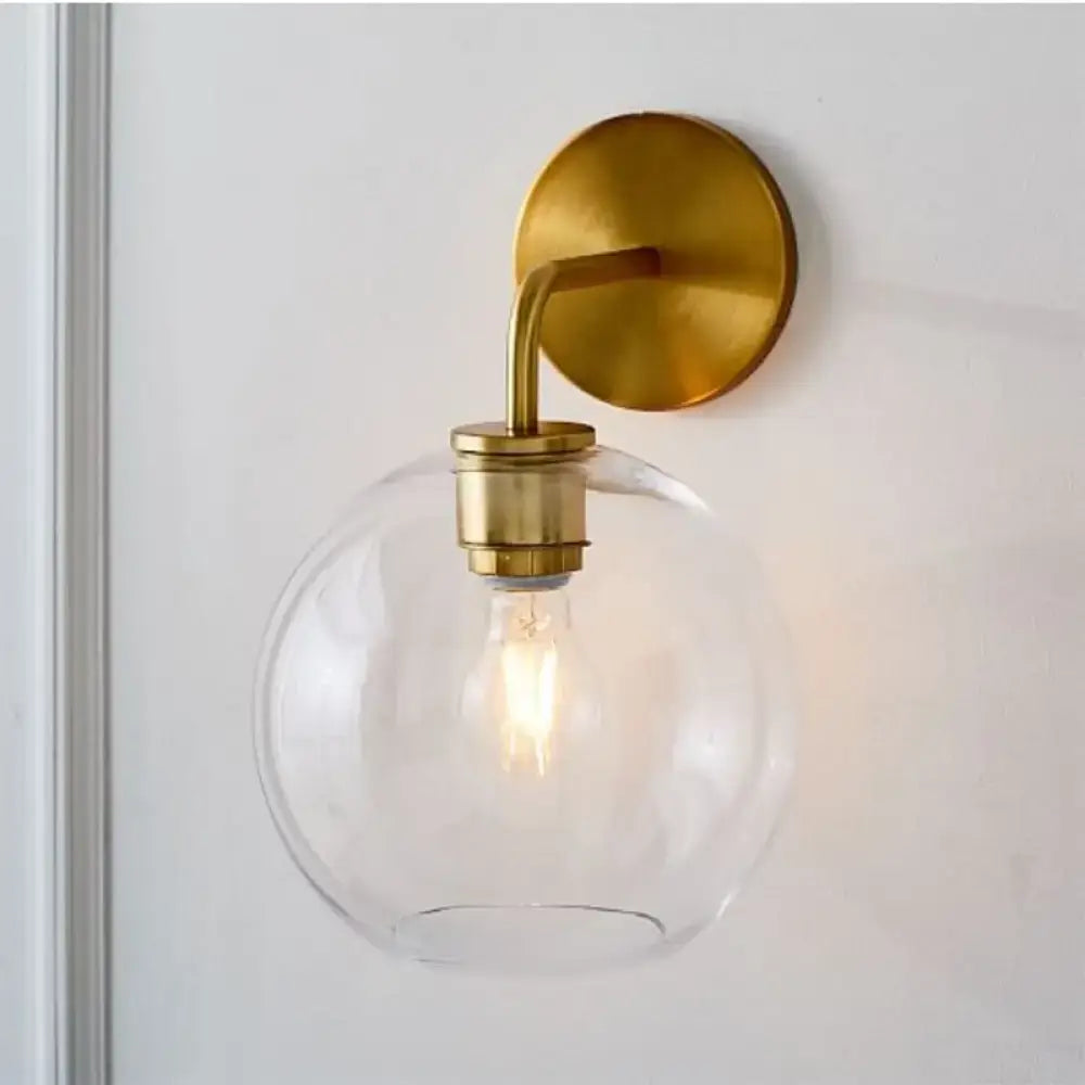 Modern brass wall lamp with sleek brass finish and clear white glass globe shade for bedroom lighting