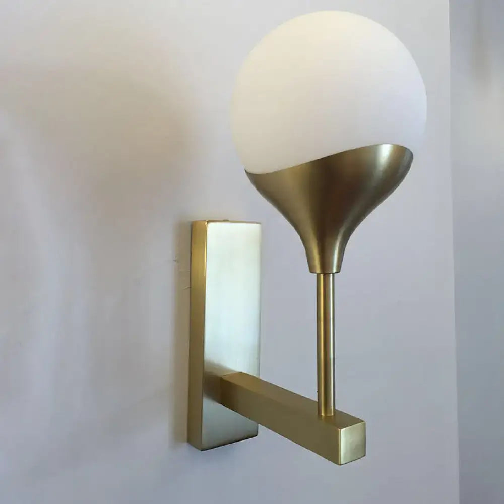 Modern brass wall lamp with a cream glass shade featuring a gold-toned metal base for bedroom wall light use