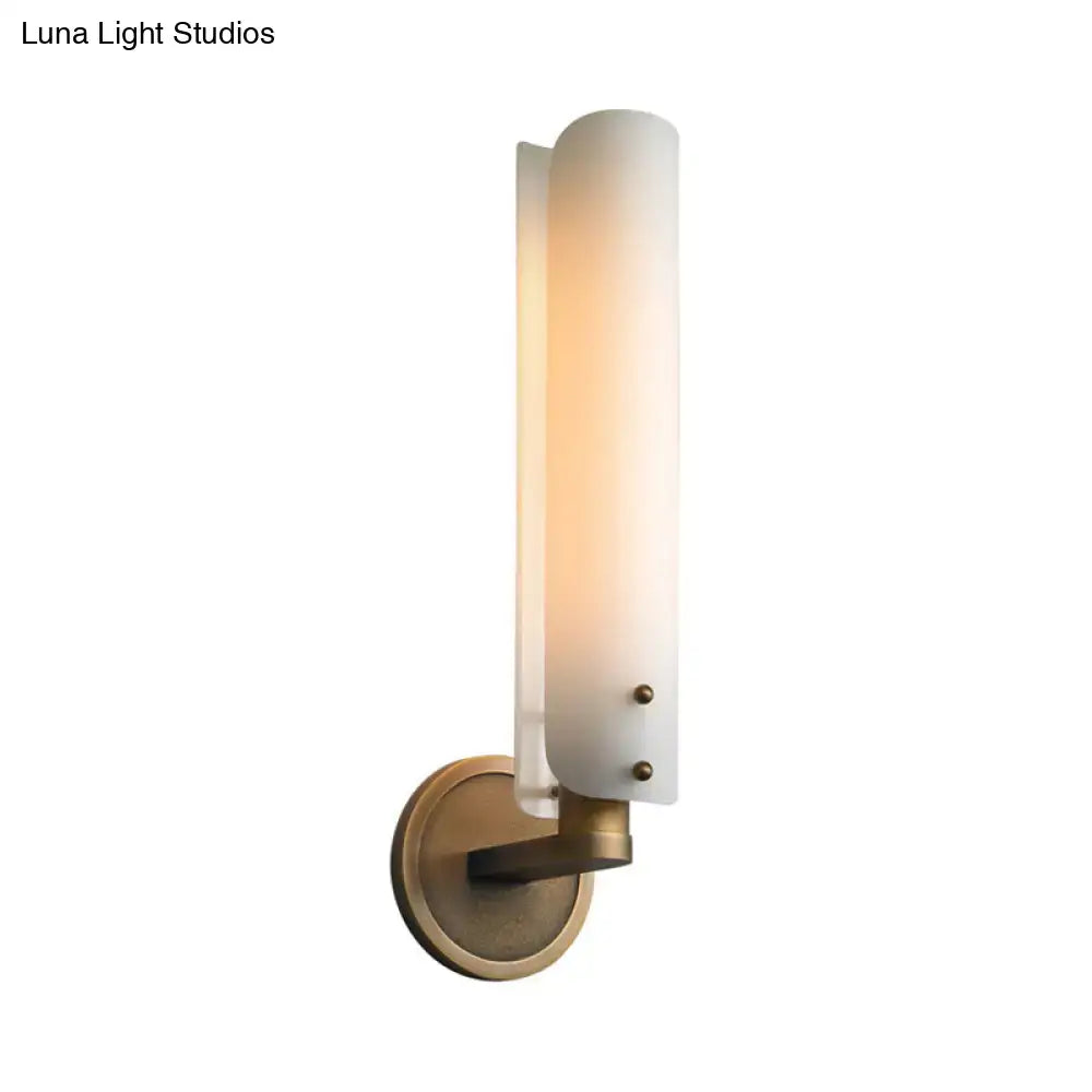 A modern brass wall lamp with a warm opal glass shade and antique brass finish for bedroom use