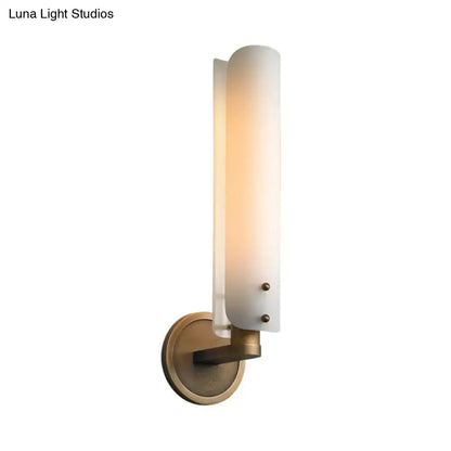 A modern brass wall lamp with a warm opal glass shade and antique brass finish for bedroom use