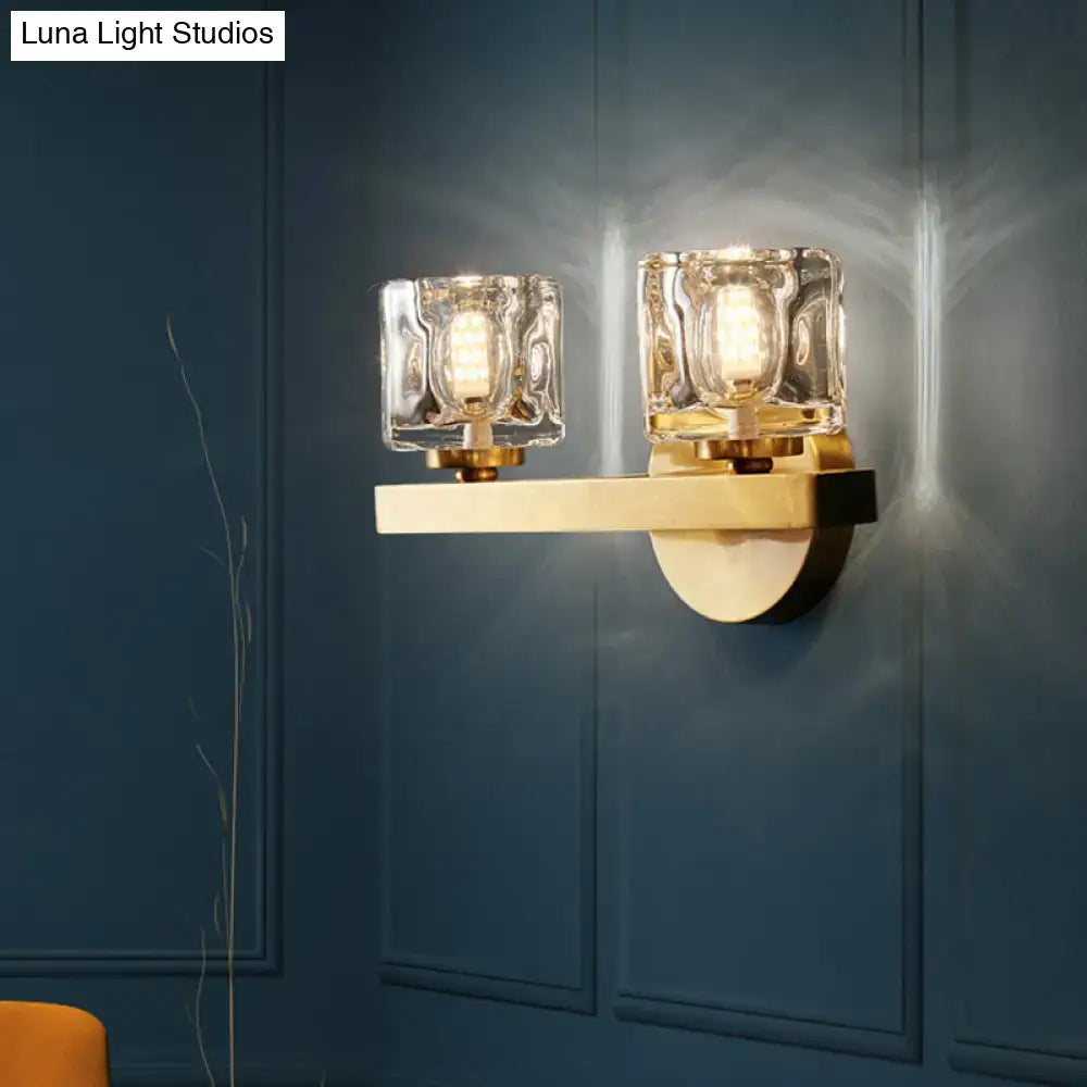 Modern brass wall light with gold-toned finish and clear crystal block featuring two textured glass shades for living room