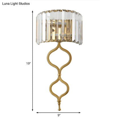Gold-toned modern brass wall sconce with crystal rectangle shade and ornate curved metal base great choice for wall mount lighting