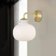 A modern brass wall sconce with an oblong milk white glass shade and decorative gold-toned rivets