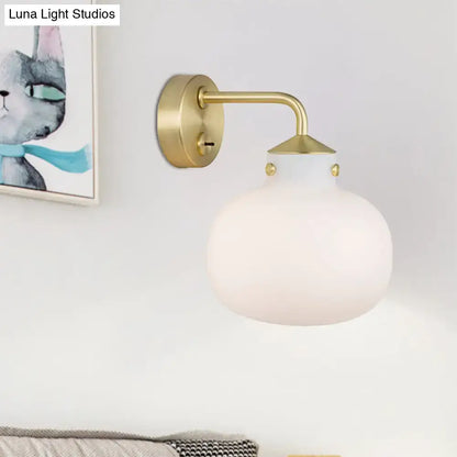 A modern brass wall sconce with oblong milk white glass shade and decorative gold toned accents for balcony lighting