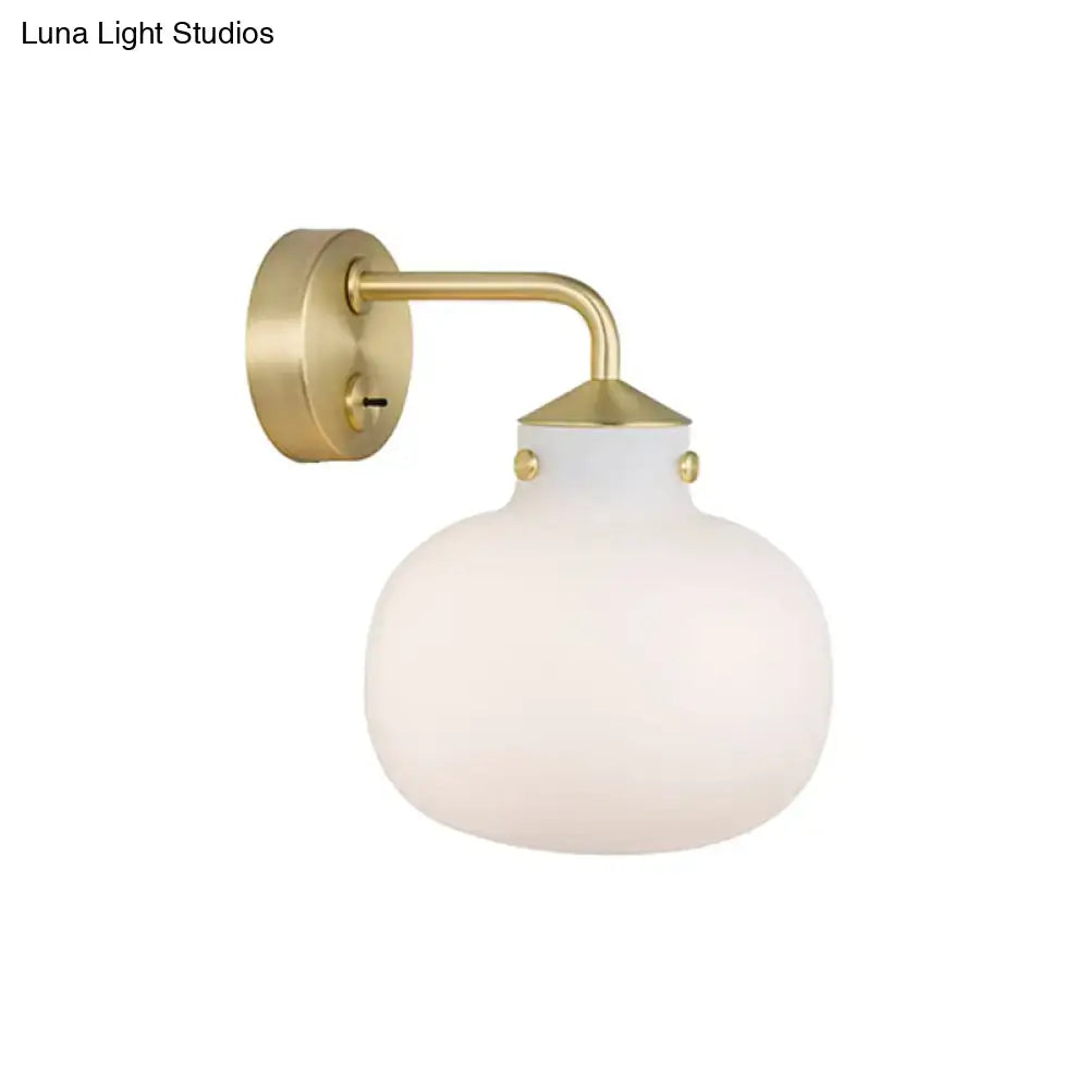 A modern brass wall sconce with oblong milk white glass shade and decorative gold-toned rivets for balcony lighting