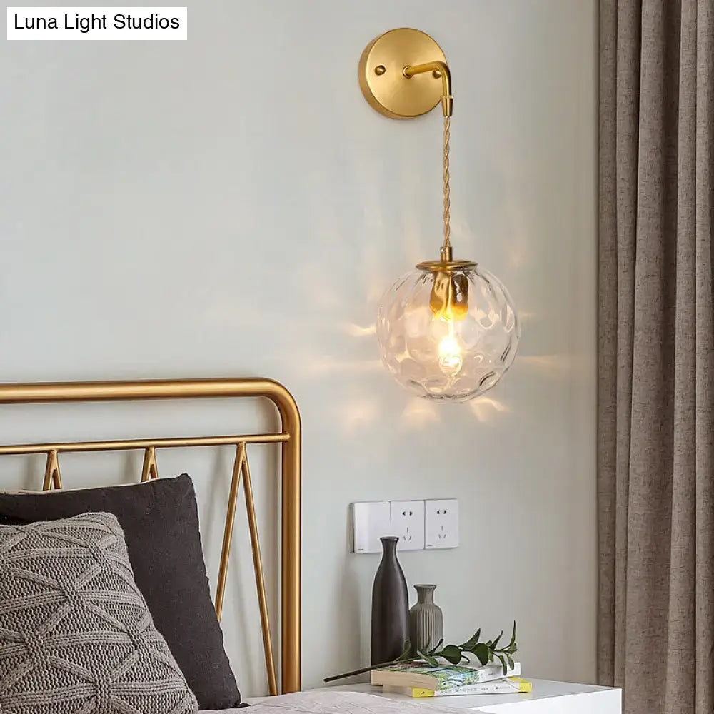 Modern brass wall sconce with gold finish and textured clear water glass shade suspended by twisted cord e12 e14