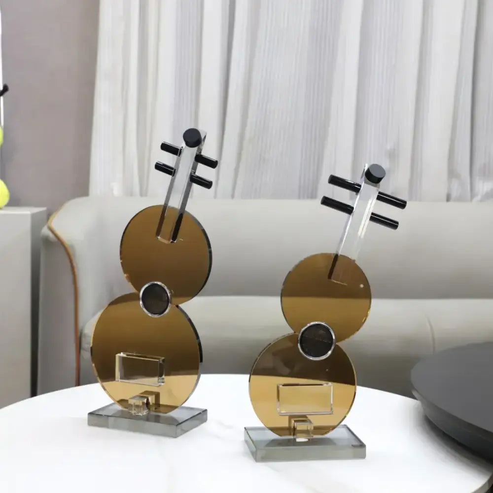 Two sleek gold toned acrylic decorbites crystal guitar sculptures with black accents and clear glass bases for living room decor