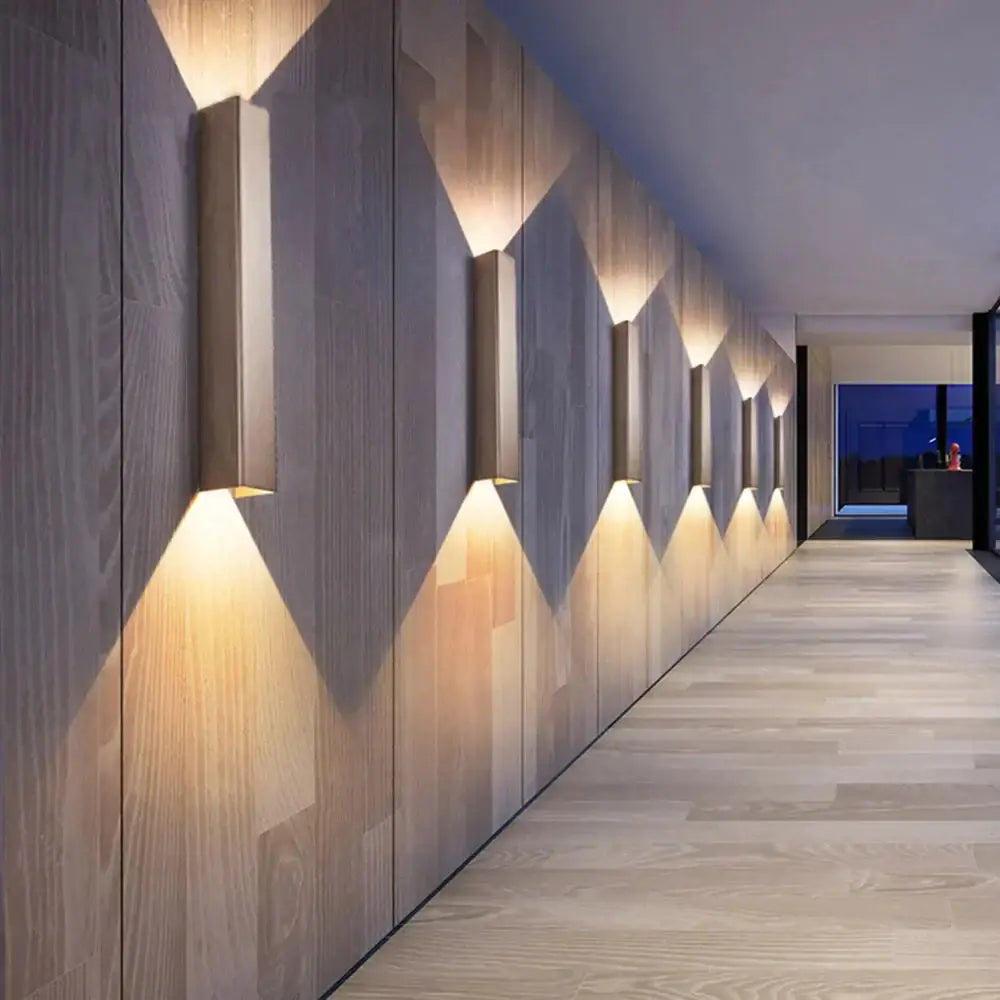 Modern brushed aluminum rectangular wall sconce with warm ambient light casting geometric shadows on wood-paneled walls