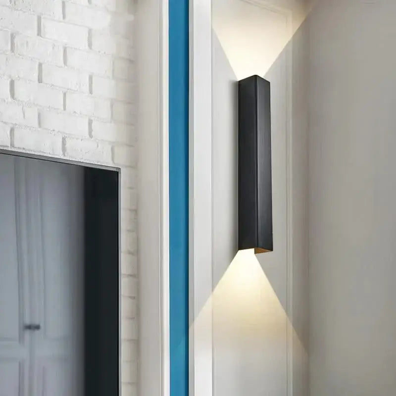 Black rectangular brushed aluminum wall sconce with matte finish and warm bottom edge light for bedroom ambient lighting