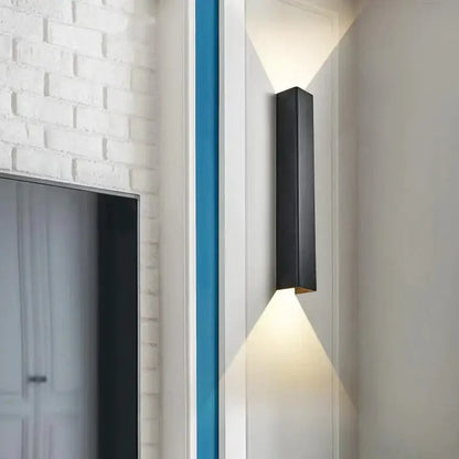 Black rectangular brushed aluminum wall sconce with matte finish and warm bottom edge light for bedroom ambient lighting