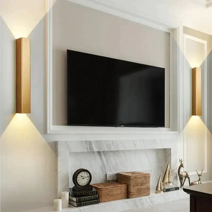 Modern brushed aluminum rectangular wall sconce in gold mounted beside black flat-screen television in white frame