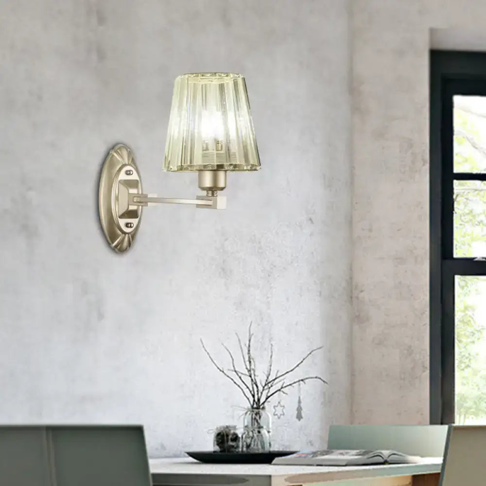 A modern brushed brass wall sconce with a faceted translucent green glass shade for bedroom wall light fixture