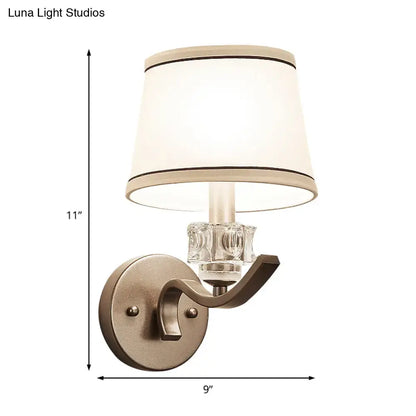 A modern brushed brass sconce light with clear crystal accent and off-white black-trimmed lampshade wall light