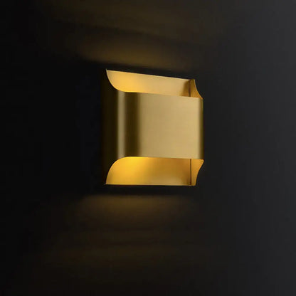 A modern brushed brass flush wall sconce with warm golden curved metallic panels for stairwell wall light use