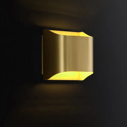 A modern brushed brass flush wall sconce with geometric design emits warm yellow glow as a stylish wall light