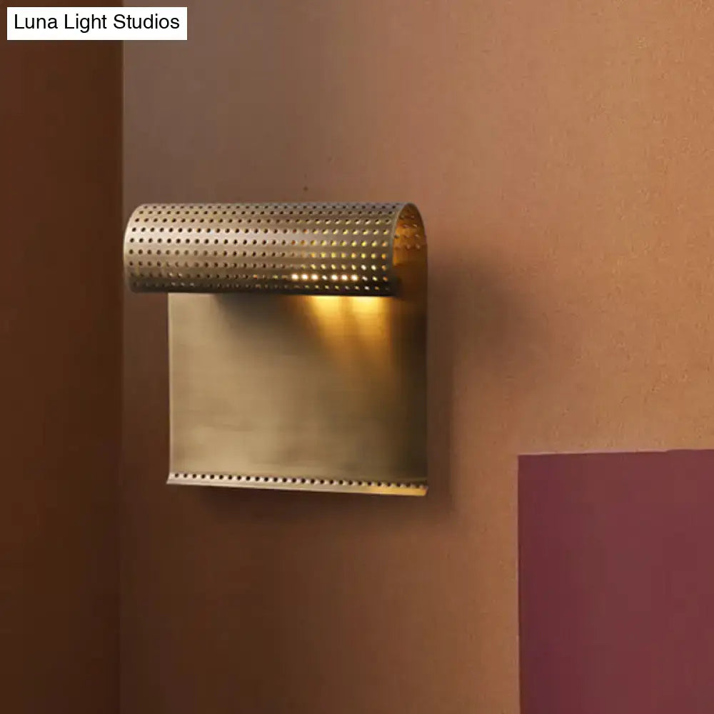 Modern brushed brass scrolled wall mounted sconce with perforated cylindrical top and rectangular base for bedroom lighting