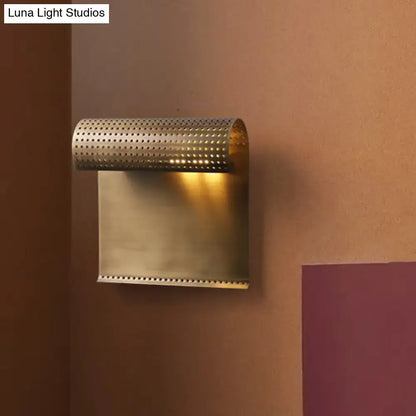 Modern brushed brass scrolled wall mounted sconce with perforated cylindrical top and rectangular base for bedroom lighting