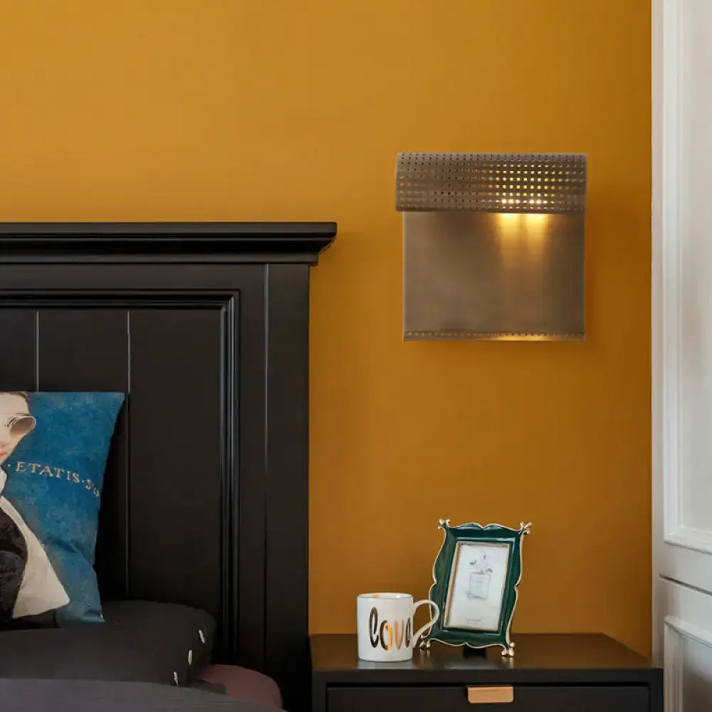 Modern wall mounted brass scrolled wall sconce with a perforated top and brushed finish for bedroom lighting