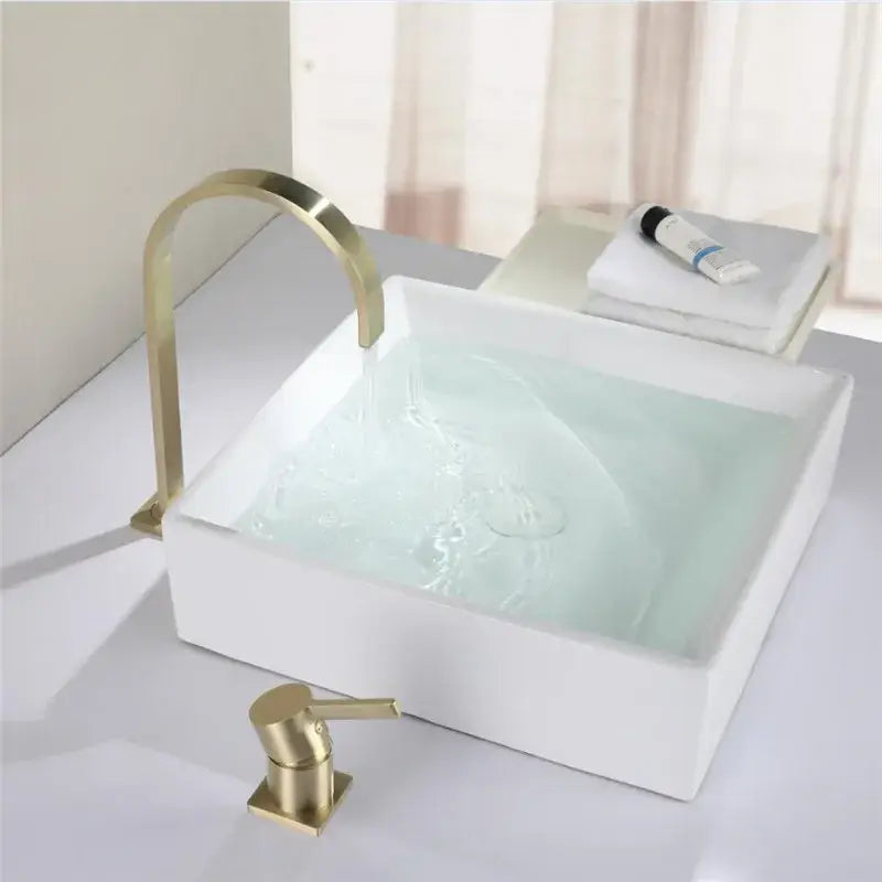 Modern brushed gold basin faucet with a sleek curved spout and soap dispenser paired with a white ceramic sink decorbites brushed gold