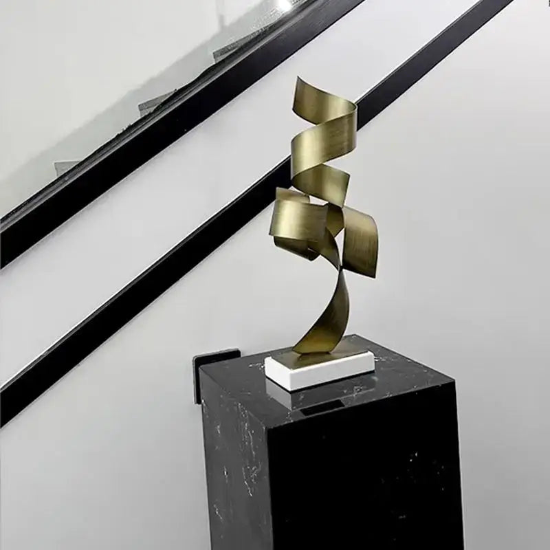 A sleek gold-toned geometric wrought iron sculpture with a flowing spiral design on a white base for living room decor