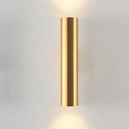 A sleek cylindrical wall lamp in brushed gold with matte black accents designed for modern bedroom lighting