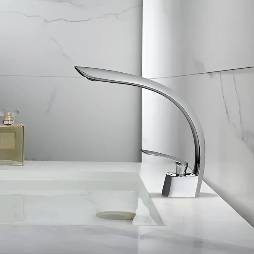 Modern chrome-finished basin faucet with sleek curved spout and square base complementing decorbites brushed gold basin design