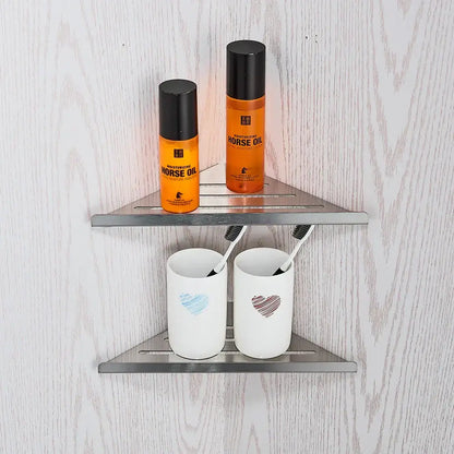 Modern brushed nickel bathroom hardware set featuring a silver triangular shower caddy with two shelves holding orange horse oil bottles and white ceramic toothbrush holders