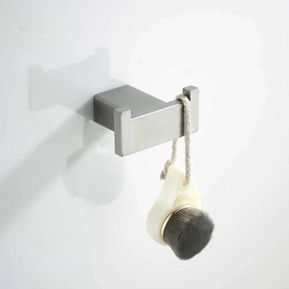 Silver rectangular wall-mounted hook holding cream bath brush with dark bristles in modern bathroom hardware set