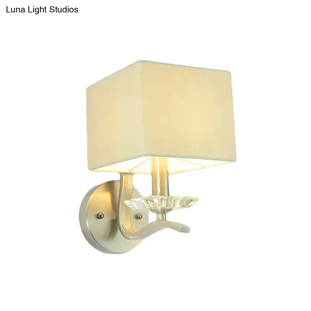 Cream-colored fabric cube bedside wall lamp with crystal accent mounted on a modern brushed nickel fixture