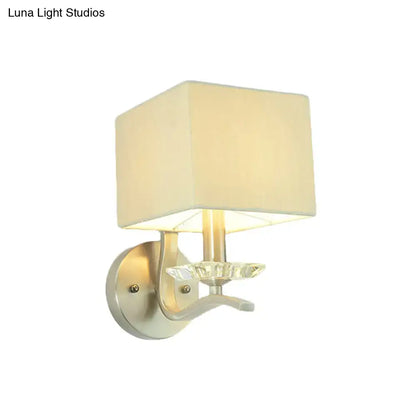 Cream-colored fabric cube bedside wall lamp with crystal accent mounted on a modern brushed nickel fixture